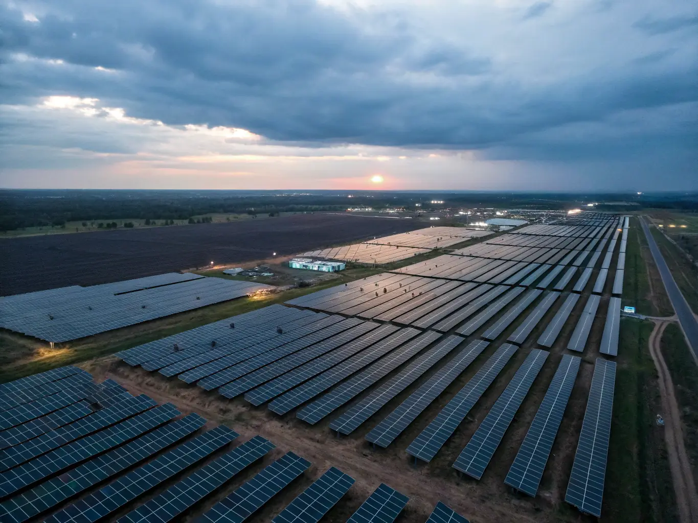 A wide shot of a solar power plant at sunset, showcasing the vast array of reflective panels concentrating sunlight onto a central receiver. The sky is a mix of orange and purple, highlighting the scale and efficiency of the operation.